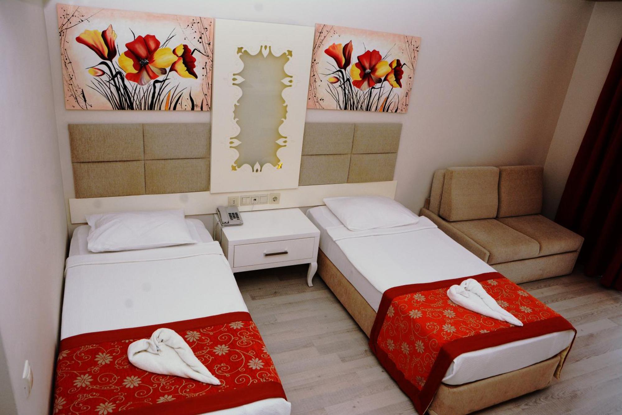 Miramor Hotel & Spa Antalia Esterno foto The photo shows a hotel room featuring two single beds with white linens, each adorned with a decorative red throw. The headboards are upholstered in a light beige fabric. Above the beds, there are two large artwork pieces depicting colorful flowers.