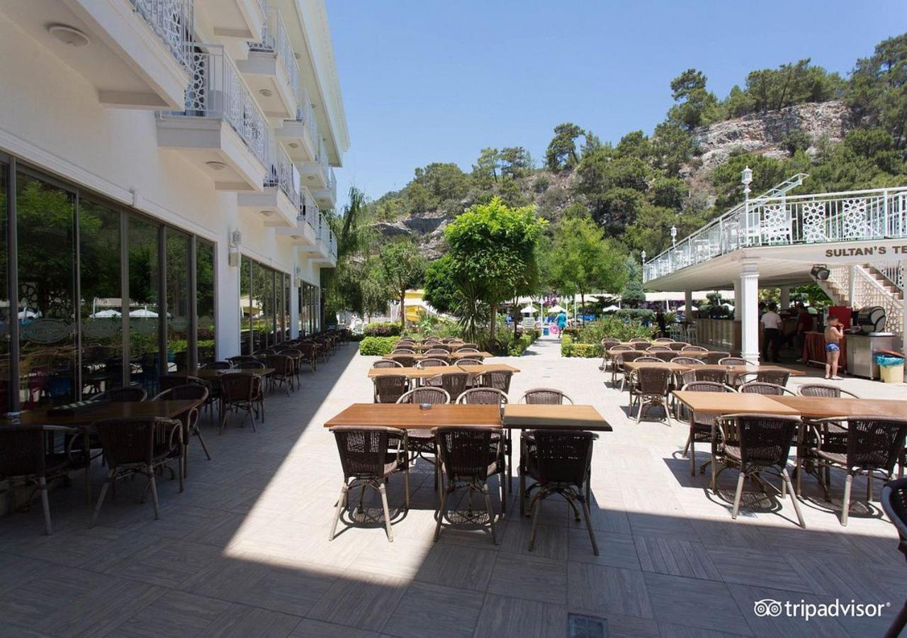 Miramor Hotel & Spa Antalia Esterno foto The photo shows an outdoor dining area, likely at a restaurant or cafe. There are several tables with chairs arranged neatly on the paved ground, and some greenery, such as trees and plants, is visible in the background. The setting appears bright an